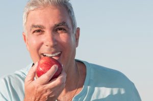 A man eats an apple with a healthy smile, kept clean with dental exams.