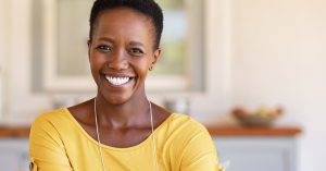 A woman wearing a yellow shirt with short hair smiles, showing off her restorative dentistry.