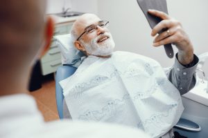 A man sits in a dental chair and admires the results of his dentistry procedure.