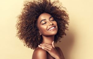 A young woman with natural hair smiles, showing off her smile that she keeps clean using dental exams.