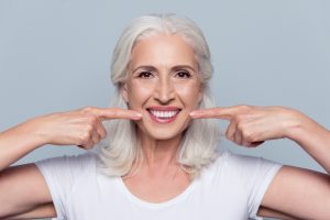 A woman points to her smile that looks beautiful after her dentist appointment.