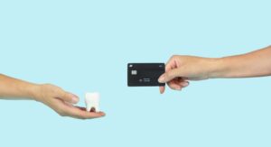 two hands holding a tooth model and a credit card